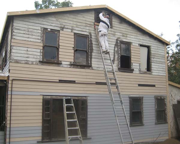 person on a ladder remodeling the exterior of a house