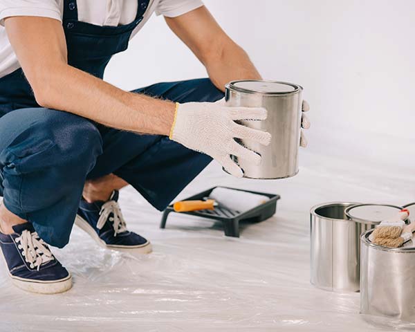 man crouched down picking up a paint can